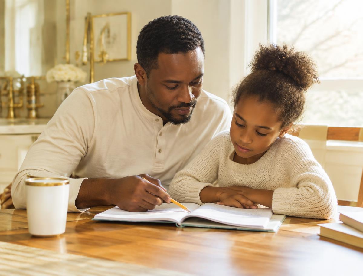 A father helps his daughter with homework at the kitchen table